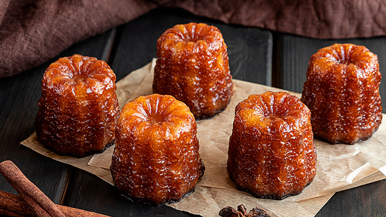 Local French dessert canele de Bordeaux served on craft paper, dark wooden background. Home bakery concept