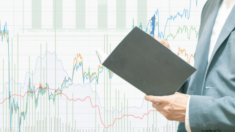 株価チャートとノートを見る男性
