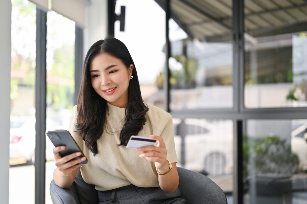 クレジットカードを手にスマートフォンを見ている女性