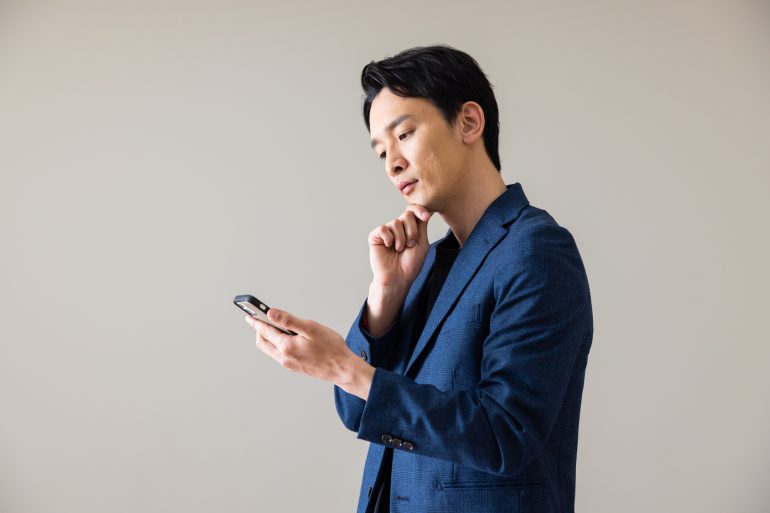 スマホをもって考え事をする人物